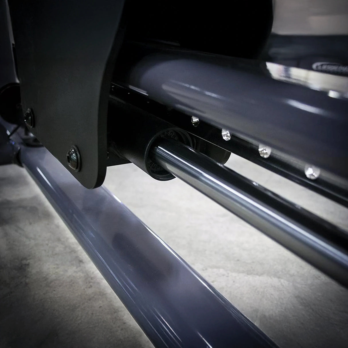 Close-up of the underside of a gym machine seat with a metal guide rod and gray frame