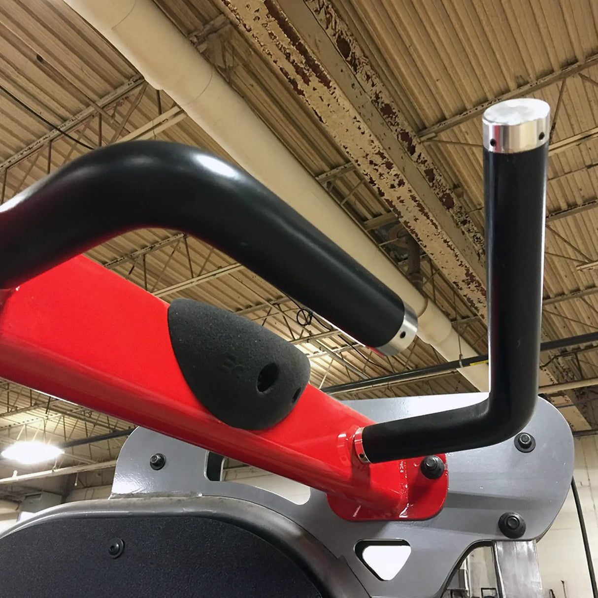 Closeup image of a red and black pull-up bar on a piece of gym equipment in a warehouse setting