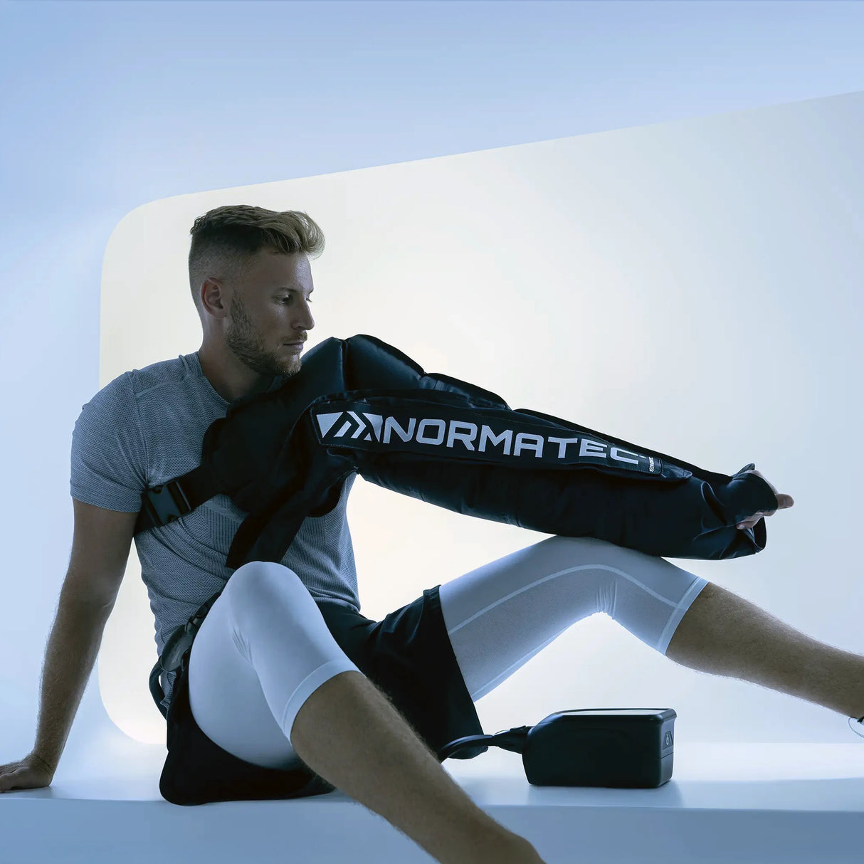 A man wearing a Normatec arm compression sleeve on his left arm.