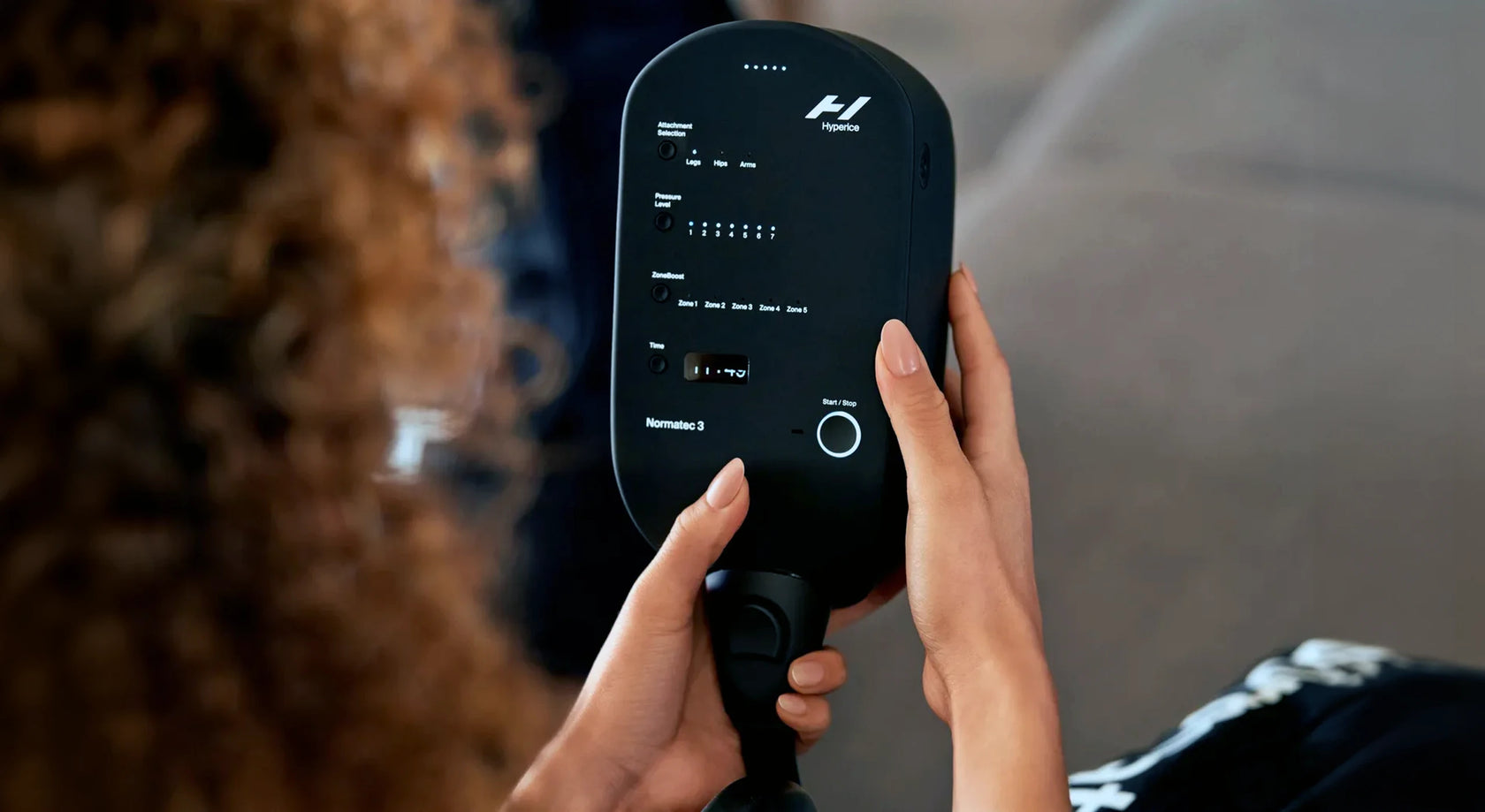Woman holding a Normatec Legs control unit in her hands.