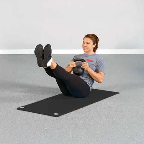 Woman doing kettlebell workout on black foam exercise mat by Perform Better