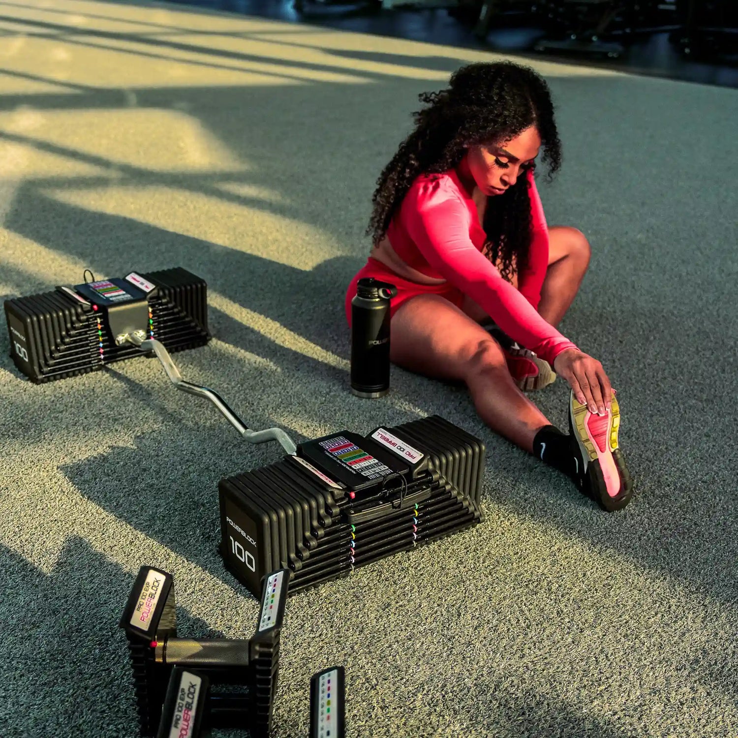 Woman stretching her calf while sitting on the floor, next to a PowerBlock EZ barbell