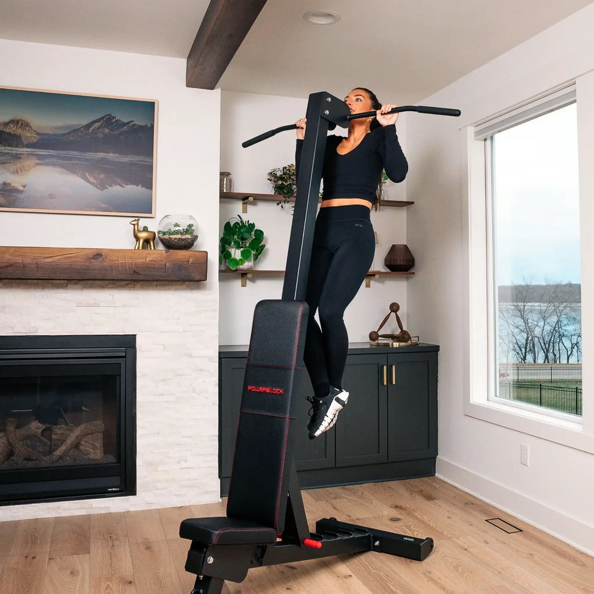 A PowerBlock bench with a chin-up attachment attached to the back which a woman is doing chin-ups on