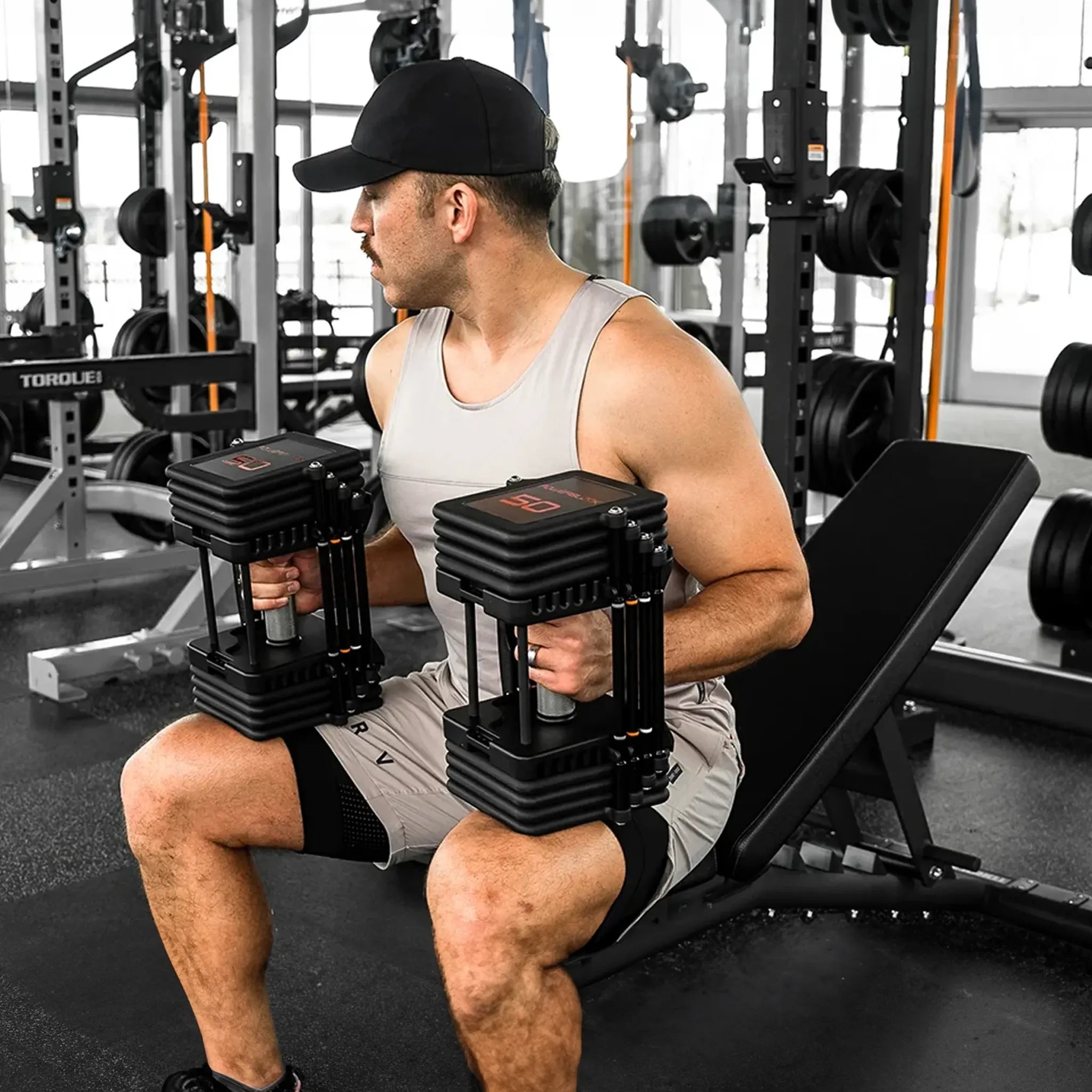 A man sitting on a bench with a pair of PowerBlock Commercial Pro 100 Dumbbells in his hands