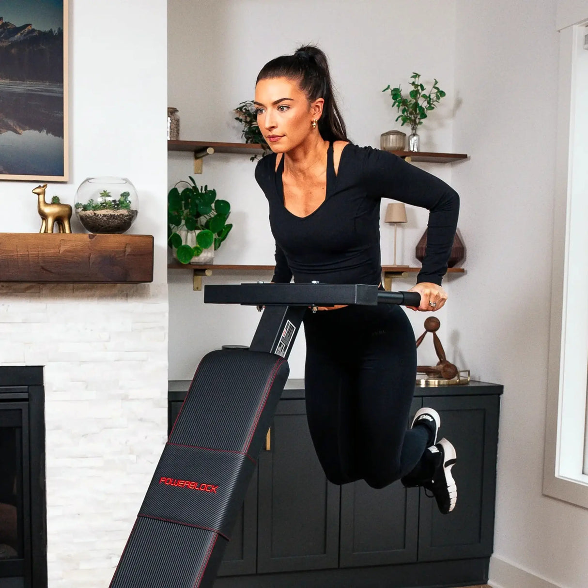 A PowerBlock bench with a dip attachment attached to the back which a woman is doing dips on