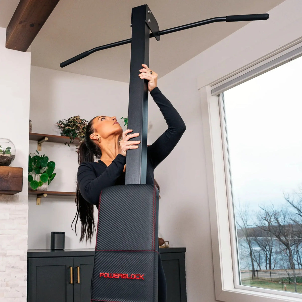 A PowerBlock bench with a chin-up attachment being attached to the back by a woman