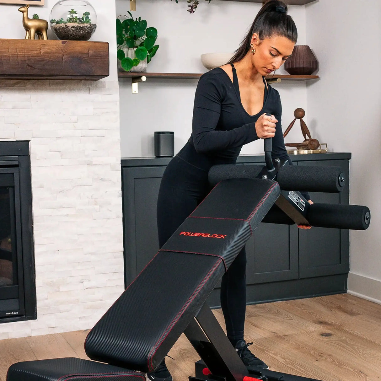 A PowerBlock bench with a sit-up ab and core attachment being attached to the back by a woman