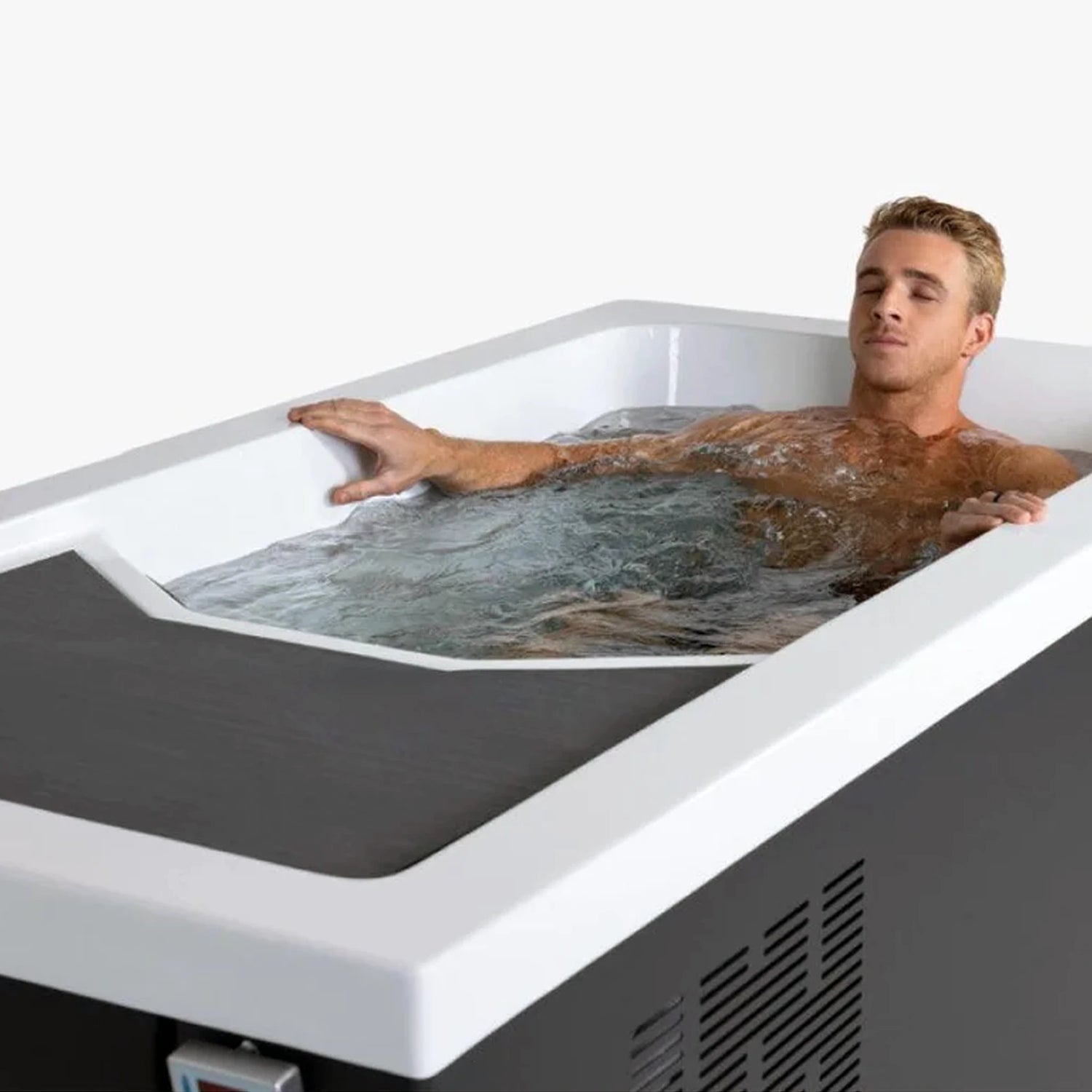 A rectangular cold plunge with a black exterior and white acrylic interior with a young man lying down inside the tub with his eyes closed