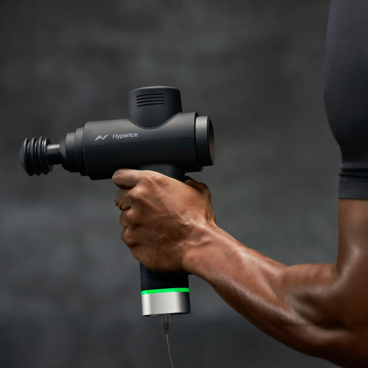 Percussion massage gun black charging cord plugged into a Hypervolt massage gun with international plug adapters