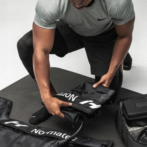 A man folding and packing his Normatec compression gear into a bag