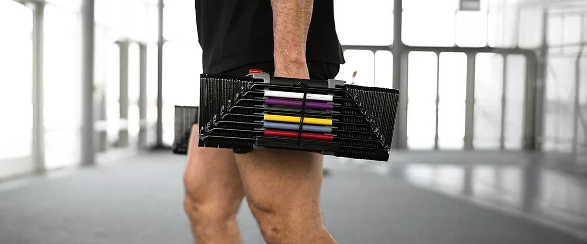 Closeup side-on image of a man wearing shorts holding an adjustable dumbbell while walking