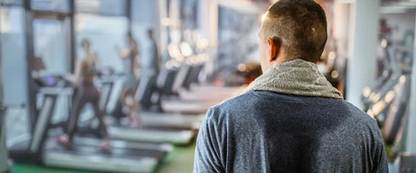 Sweaty man walking through a gym with a towel around his neck