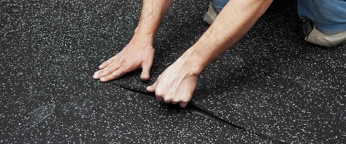 Closeup image of a man on his knees installing a rolled rubber floor