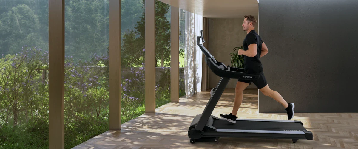 A man running on a treadmill in a beautiful home looking through some large windows out into a lush yard