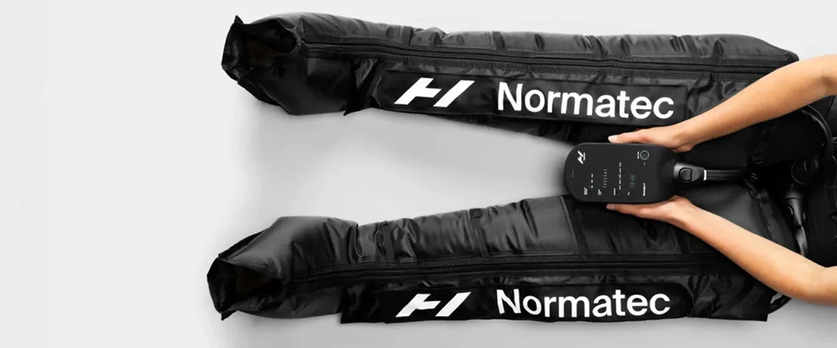 A birds eye view of someone's legs stretched out flat on the floor wearing Normatec legs.