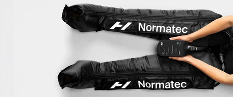 A birds eye view of someone's legs stretched out flat on the floor wearing Normatec legs.