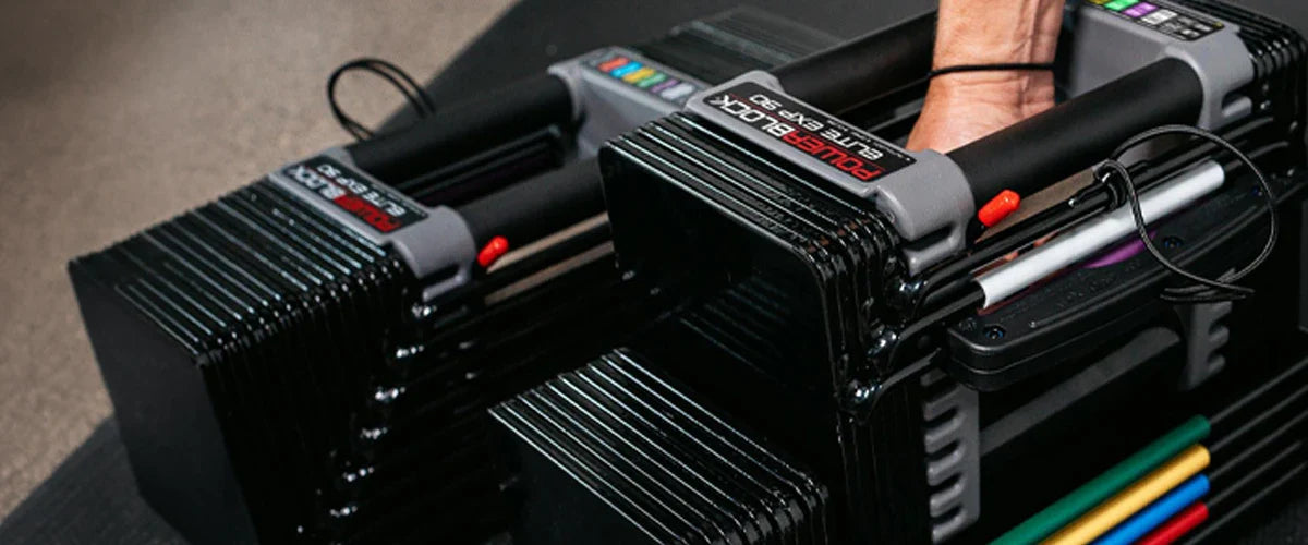 Closeup photo of a pair of PowerBlock dumbbells on the ground with a hand picking one up