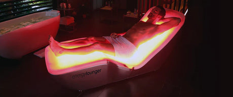 Man lying on the Energy Lounger red light bed with one hand behind his head and his eyes closed