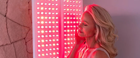 Woman touching her face with her eyes closed while standing in front of a red light therapy panel