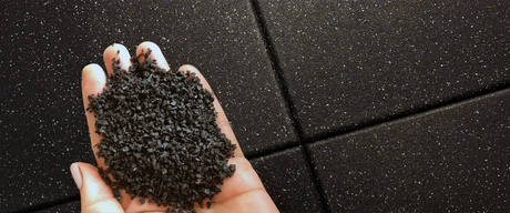 A mans hand with the palm up holding black rubber granules with a black rubber tile background under his hand.