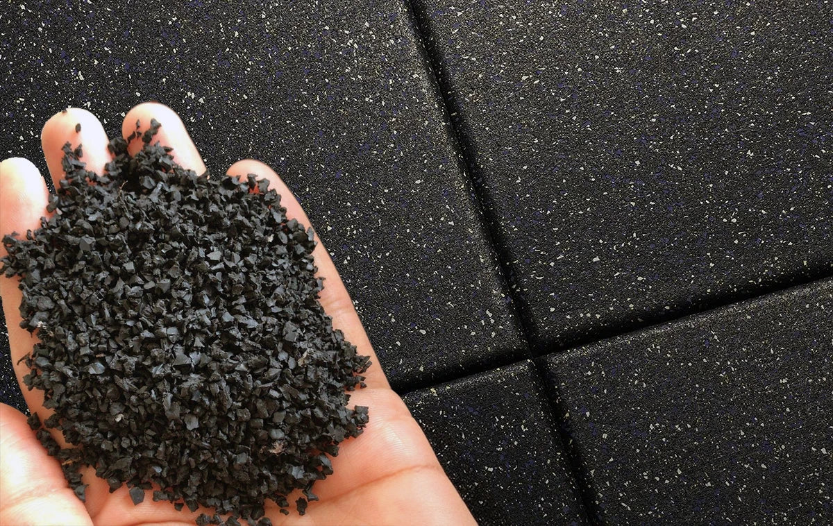 Black rubber floor tiles in the background with a mans hand holding rubber granules in the foreground
