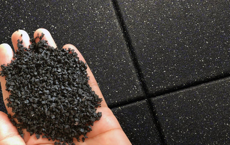 Black rubber floor tiles in the background with a mans hand holding rubber granules in the foreground