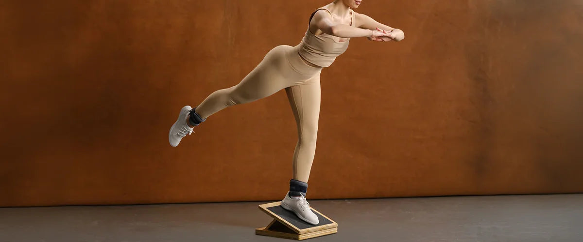 Woman balancing on one leg on a slant board in an empty room with a brown back wall