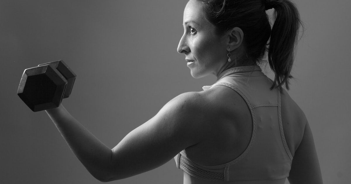 grayscale of woman carrying dumbbell