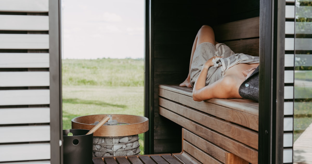 Person relaxing in a wooden sauna with outdoor view.