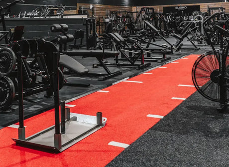 A gym full of equipment with a red strip of artificial turf running down the middle of the room.