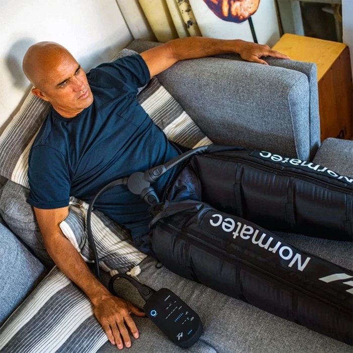 Kelly Slater lying on a couch wearing Normatec 3 Legs