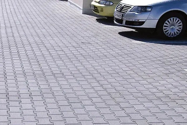 An outdoor parking lot with two cars parked on the rubber paver surface making up the parking lot