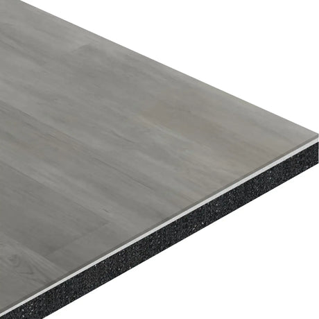 A close-up of the ECORE Athletic Baller Rally Laminate Roll - 14mm Class 2 Flooring shows its rectangular, gray wood-look surface and black core, angled to display the layered construction.