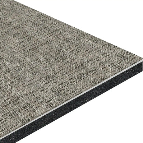 A close-up of the ECORE Ebb & Flow Motivate Laminate Roll - 6mm Class 1 Flooring by ECORE Athletic shows its textured woven gray surface and dark solid core, displayed at an angle to emphasize its thickness and layered construction.