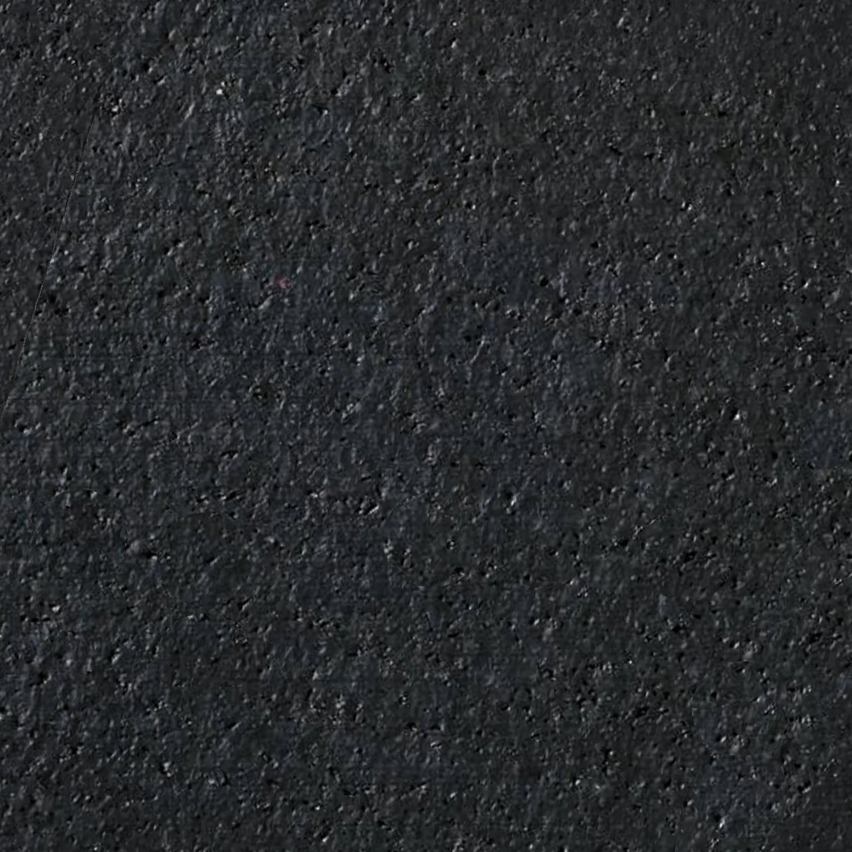 Close-up of ECORE PlayGuard Rubber Tile - 2.5" Playground Flooring by ECORE Athletic, showing its rough, dark textured surface with small specks and uneven areas throughout.