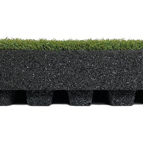 A close-up side view of the ECORE RageTurf dBTile - 2.5" Athletic Turf Tile by ECORE Athletic shows artificial grass on top, a thick textured black rubber layer in the middle, and evenly spaced black rubber feet at the bottom.