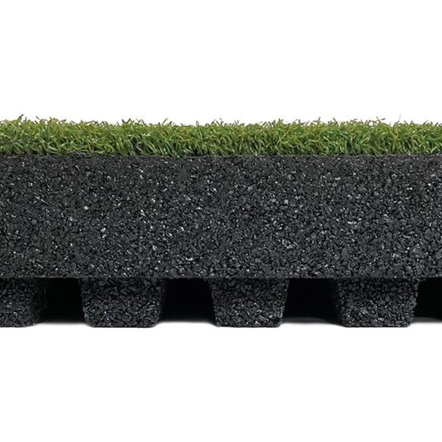 A close-up side view of the ECORE RageTurf dBTile - 2.5" Athletic Turf Tile by ECORE Athletic shows artificial grass on top, a thick textured black rubber layer in the middle, and evenly spaced black rubber feet at the bottom.