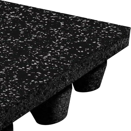 Close-up of the corner of an ECORE Athletic Performance dBTile Rubber Tile - 2.5" Acoustic Flooring, featuring thick black rubber with white speckles and elevated by cylindrical rubber feet underneath.