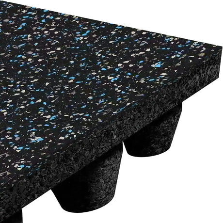 Close-up of the ECORE Athletic Performance dBTile Rubber Tile - 2.5" Acoustic Flooring, featuring a thick black mat with blue and white speckles, textured surface, and cylindrical supports visible beneath the raised corner.