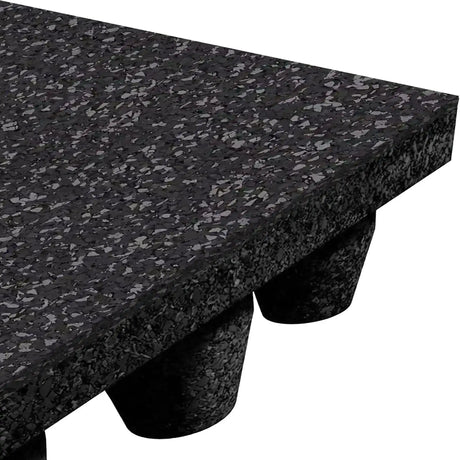 Close-up of the ECORE Athletic Performance dBTile Rubber Tile 2.5" Acoustic Flooring—thick, speckled black with beveled edges and cylindrical feet underneath, forming an elevated platform.