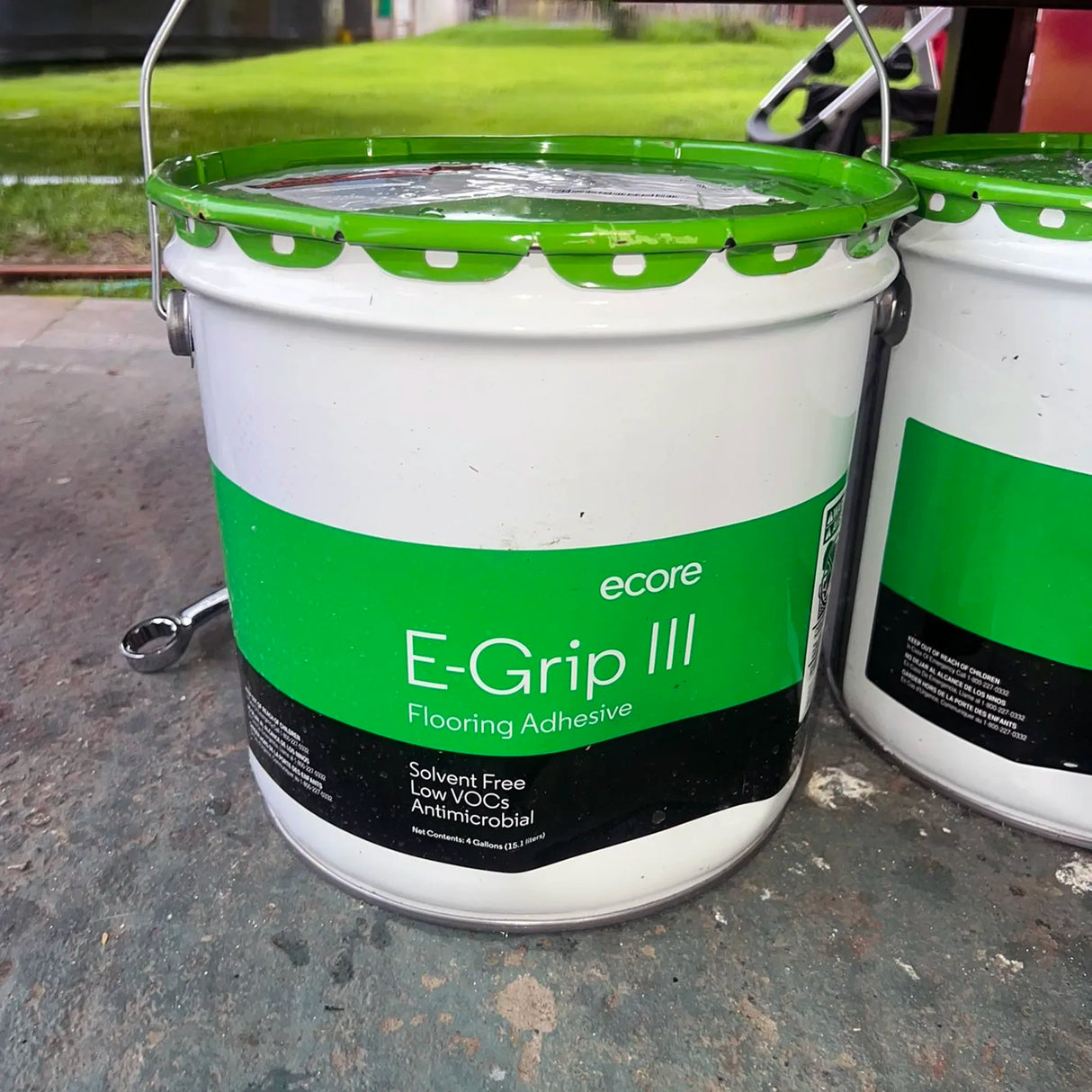 Two buckets of ecore E-Grip III Flooring Adhesive on a concrete surface.