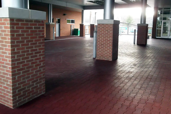 An outdoor covered foyer between two buildings with red rubber pavers making up the floor