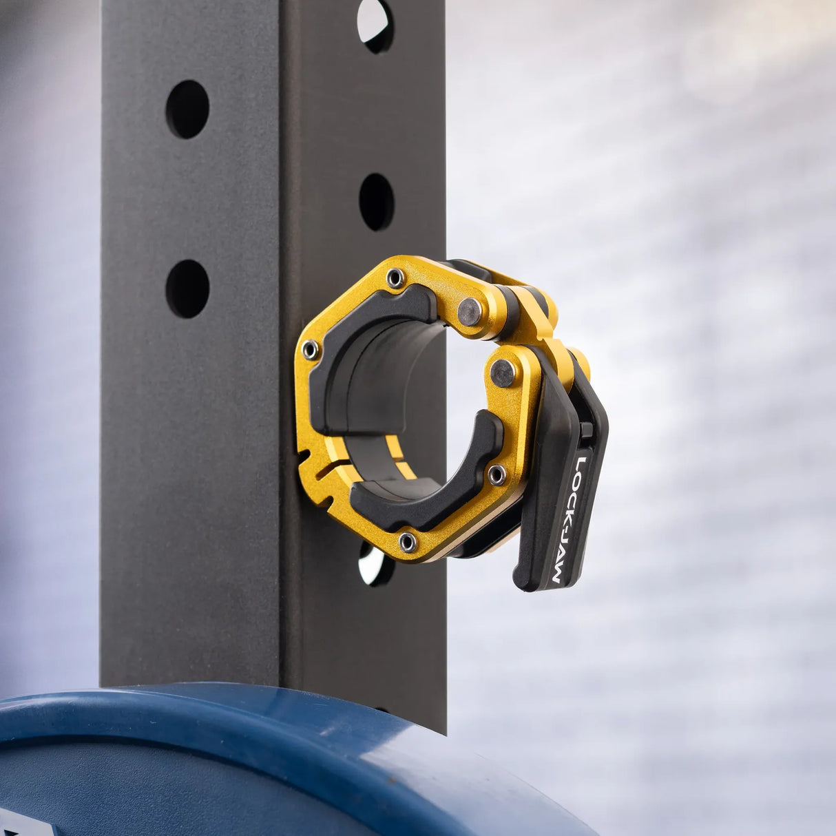 A black and gold Lock-Jaw metal barbell collar with visible branding and magnets on the inside stuck to the side of a steel beam.