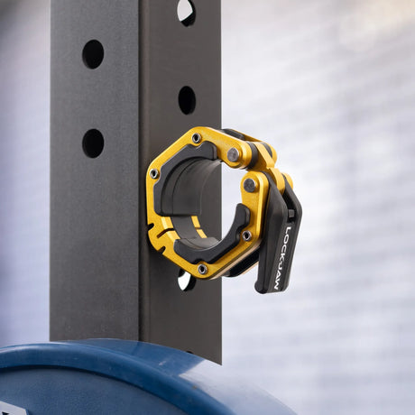 A black and gold Lock-Jaw metal barbell collar with visible branding and magnets on the inside stuck to the side of a steel beam.