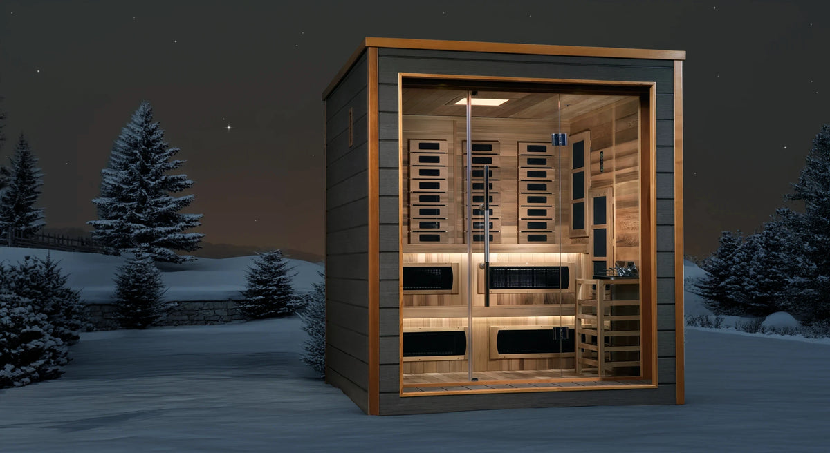 Karlstad model sauna with a hybrid full spectrum infrared tradition sauna design and a 3 person capacity made from Canadian red cedar on the interior and dark all weather composite on the exterior built for outdoor use sitting in a snowy yard at night