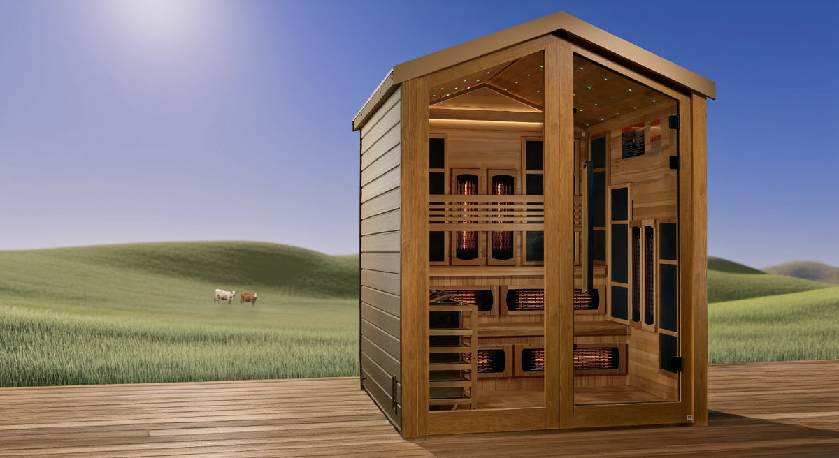 Golden Designs Kaskinen hybrid model sauna featuring full spectrum infrared and traditional steam technology with star galaxy overhead lighting made from Canadian red cedar interior and an all weather composite exterior with a 6 person capacity built for outdoor use positioned on a deck overlooking a grassy meadow with two cows on it