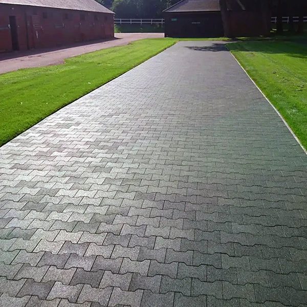A long wide path made of green rubber pavers outside with some grass and buildings around