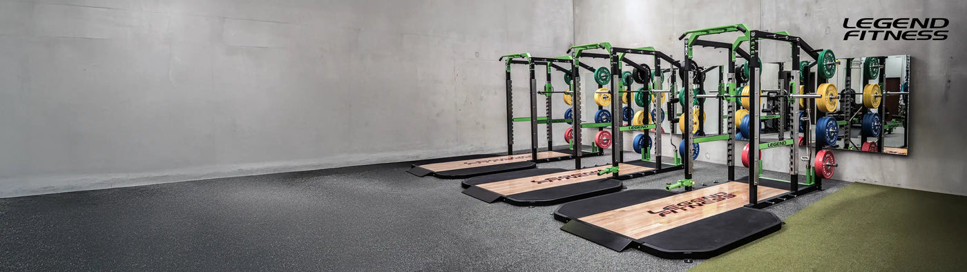 Large gym with three green legend fitness racks with wooden platforms, green artificial turf, and a rubber floor.