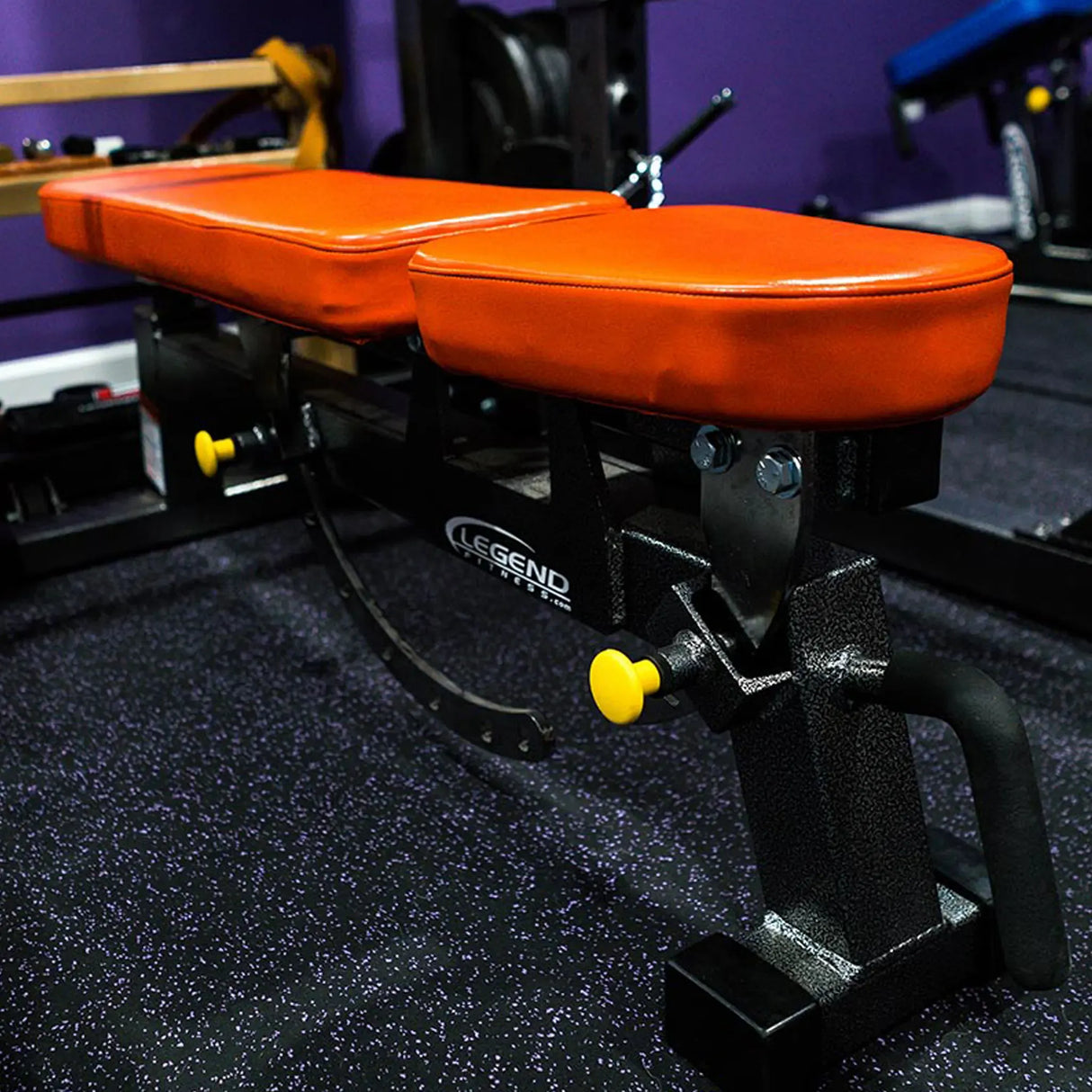 Orange and black gym bench with 'Legend Fitness' branding on a dark floor.