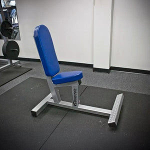 The Legend Fitness 3104 Multi-Purpose Bench by Legend Fitness, featuring blue padding and a silver frame, is placed on black rubber matting in a gym near a wall and weight rack.
